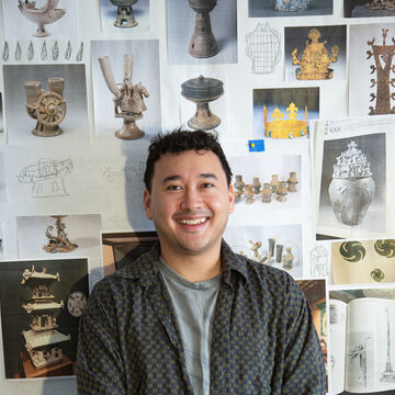 SAIC faculty member Anthony Park Kascak, a person with light skin tone and dark hair, standing against a wall full of pictures of ceramics and sculptures.