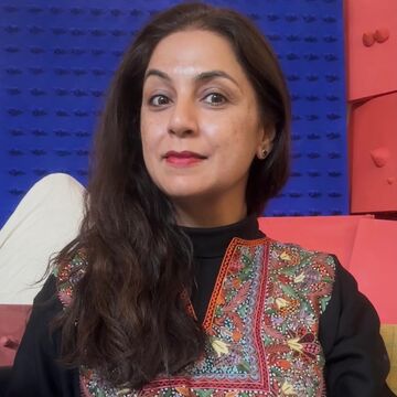 Portrait of Gunjan Chawla Kumar, a Southeast Asian person with a medium skin tone and long brown hair, posing in front of a blue and red background.