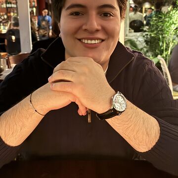 Portrait of Juan Pablo, an adult with short dark hair and a medium-fair skin tone, seated at a table.