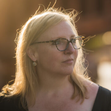 SAIC faculty member Melinda Whitmore, a person with light skin tone, light hair and glasses standing outside.
