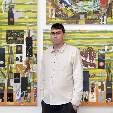 SAIC faculty member Jasper Goodrich, a person with dark hair, light skin tone, and glasses, standing in front of artwork.