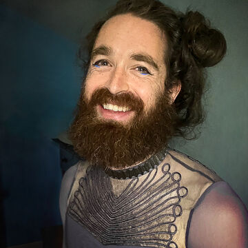 Selfie of nyla, an adult person with a fair skin tone, long dark straight hair, and a beard. 