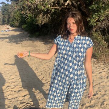 Cedar Heffelfinger, an adult person with a fair skin tone and brown hair, holding an orange on the beach. 