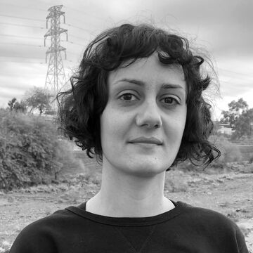 A black and white photograph of Visiting Practitioner Nazafarin Lotfi, a person with dark curly hair, standing outside.