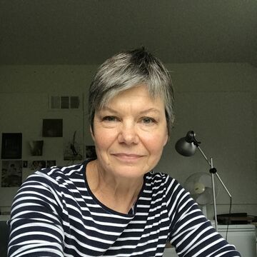 CAPX Director Kate Schutta, a person with light skin tone and short gray hair, seated at a desk in a bright office.