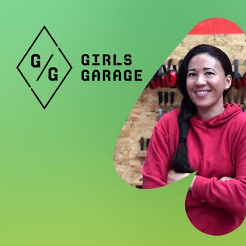 Emily Pilloton-Lam stands with arms crossed, smiling, in front of a wall of tools inside the Girls Garage workshop. The Girls Garage logo appears to the left against a green background.