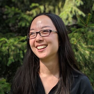 Shelley Dodson, an adult Asian person with a fair skintone, dark hair, and glasses, smiling outdoors. 