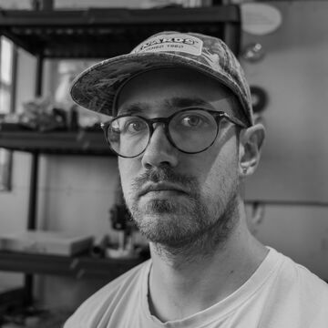 Black and white headshot of Johnny Doley, an adult person with a fair skintone and glasses. 