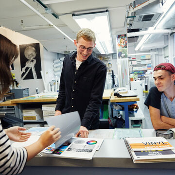 Three students of varying skintones and genders gathered around a counter. 