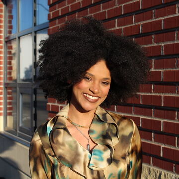 Portrait of De'Lana Sanders, an adult Black person with a medium skintone and afro, outdoors. 