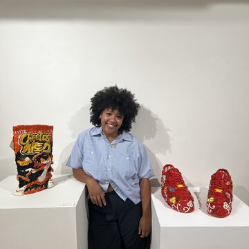 A person stands in front of a gallery display with ceramic shoes.