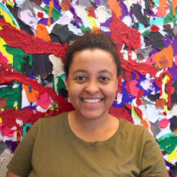 A photo of a young woman standing in front of a brightly painted canvas