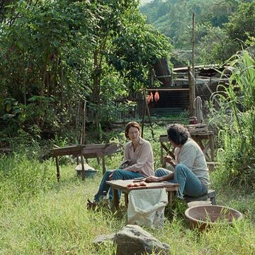 Two people talking at a small table in lush green nature.