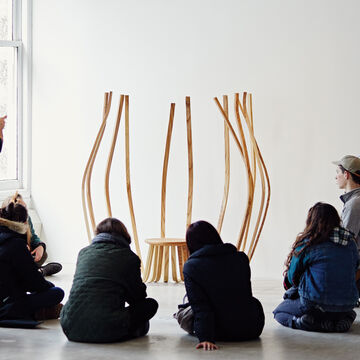 A group of students sitting in an art room looking at an art sculpture while the professor is explaining.