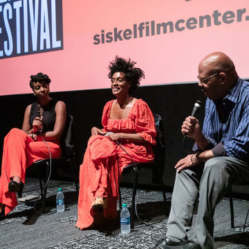 Three panelists sit in front of a movie theater screen