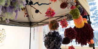 Various, colorful pompoms strung up on the frame of a tent in a gallery space.
