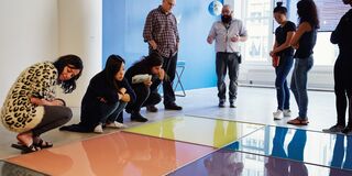 Arts Admin students listening to instructor in gallery space while looking at large, brightly colored tiles on floor.