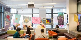 A group of students sit below fabric art in a campus space