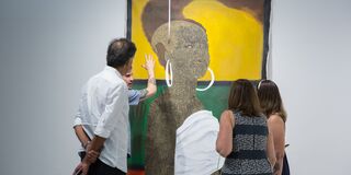Four people look at a large painting hanging in a gallery.