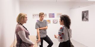 A photo of three people standing in front of some art in a white room