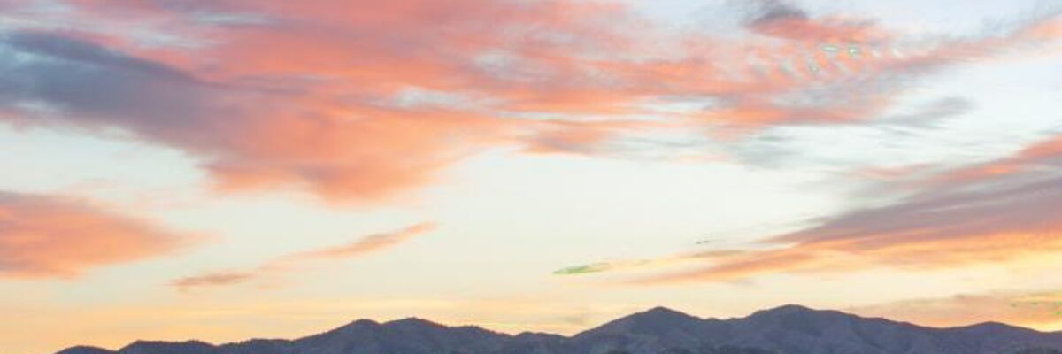 Mountains and a grassy hillside under a pink and orange sunset.