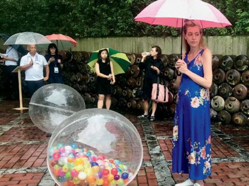 Visitors looking at clear balls filled with multicolored balls in an outdoor gallery space