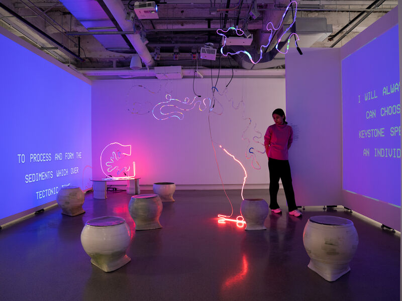 A person stands amongst a group of neon pieces and blue projections