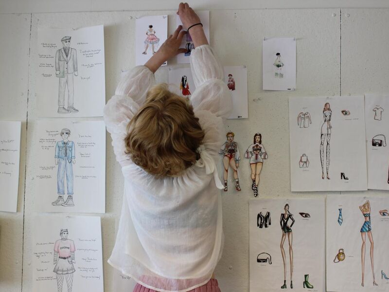 A student pinning up a sketch on a wall of various drawings of outfits.