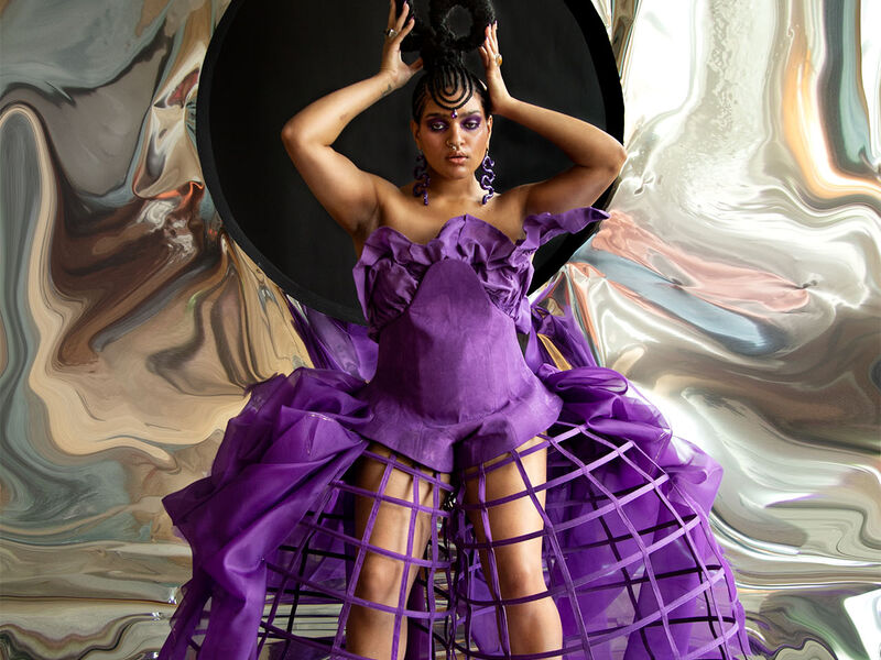 A person in an ornate purple dress on a reflective backdrop