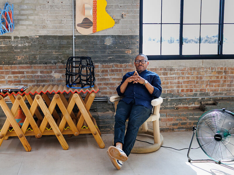 Portrait of Norman Teague, an adult Black person with a medium-dark skin tone, seated in his studio space.. 