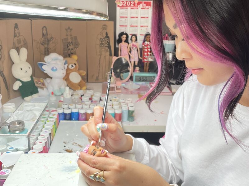 Minh-Tam Nguyen painting a Barbie doll head. 