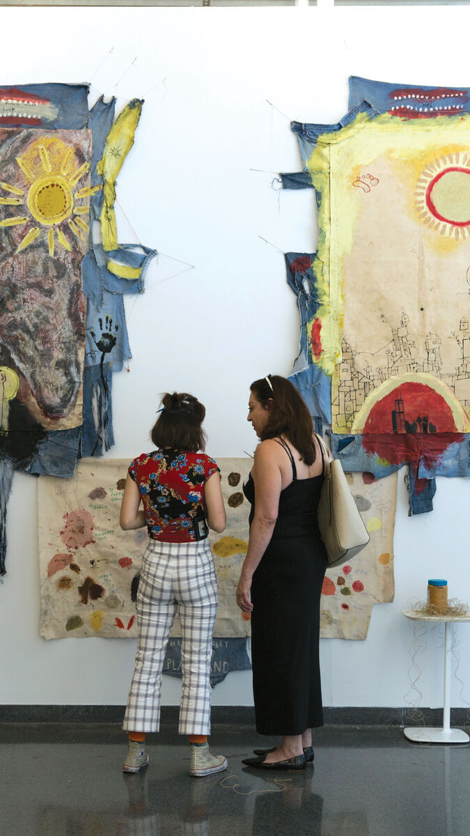 Two people looking at large pieces of hanging wall art outside of a gallery. 