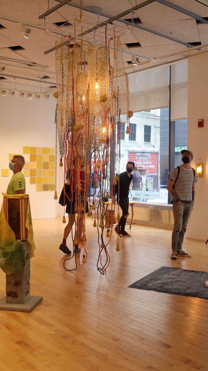 A group of people in a gallery with a large hanging piece of art in the center of the room. 