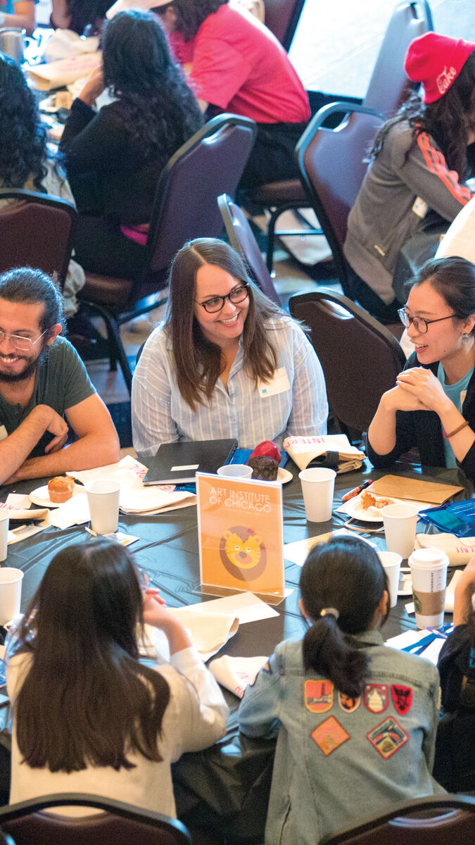 A group of students talking while seated at a large round table. 