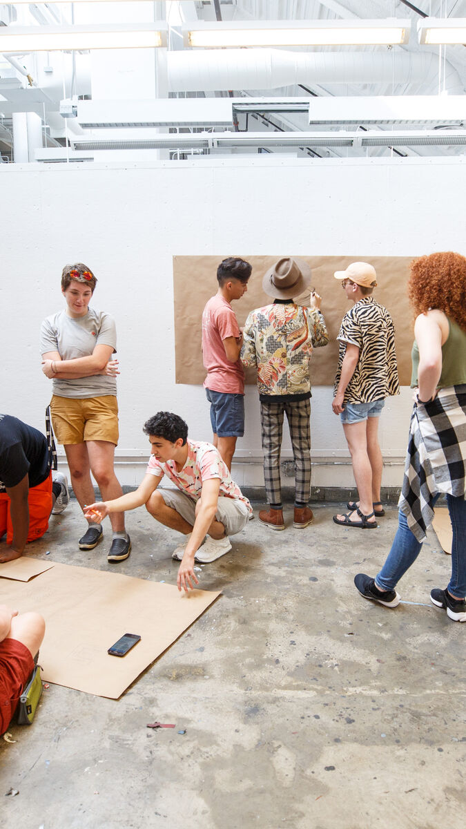 A group of students writing and making on brown parchment paper in an open gallery. 