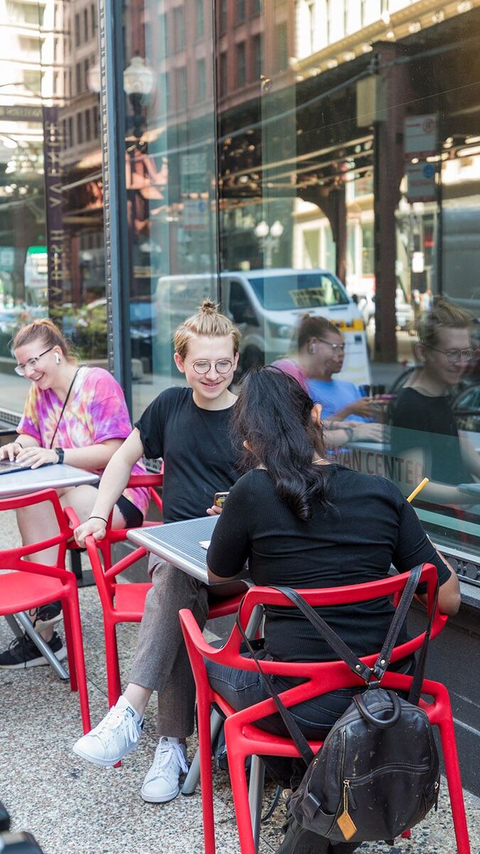 Students sitting at cafe tables outside reading, talking, and working.