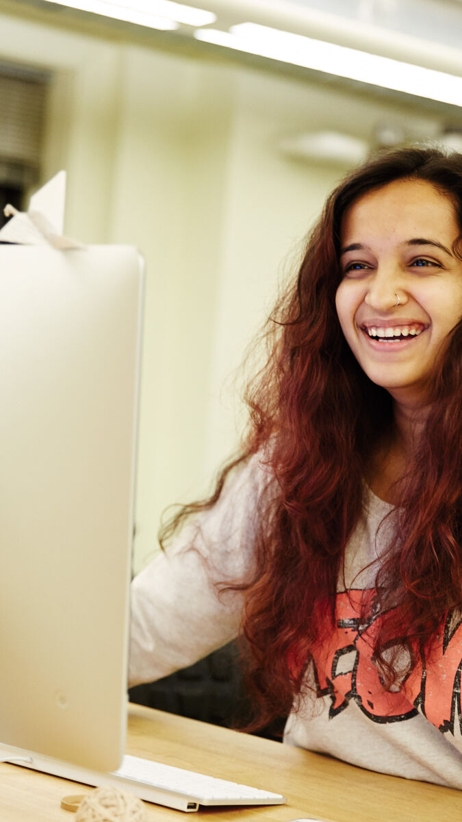 A student sits behind a computer and smiles.