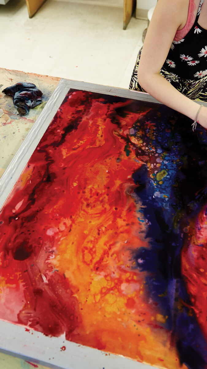 A student painting with bright red and blue on a large canvas.