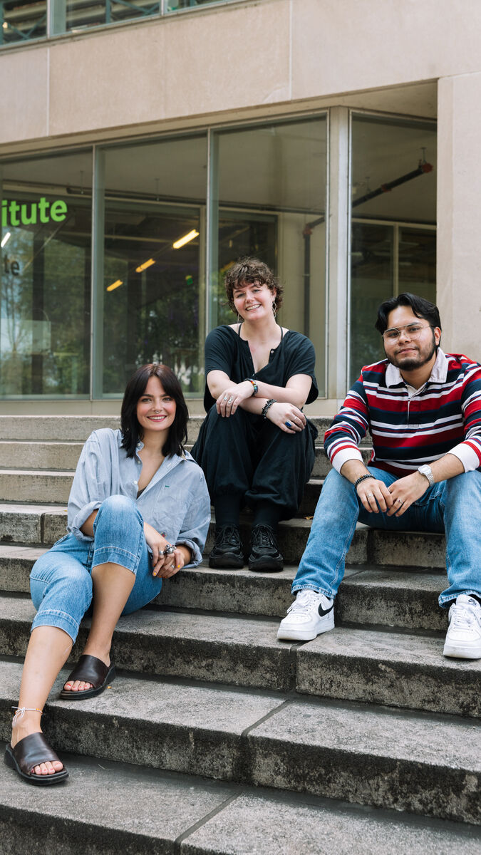Three SAIC students smile as they sit on the steps of SAIC's campus.