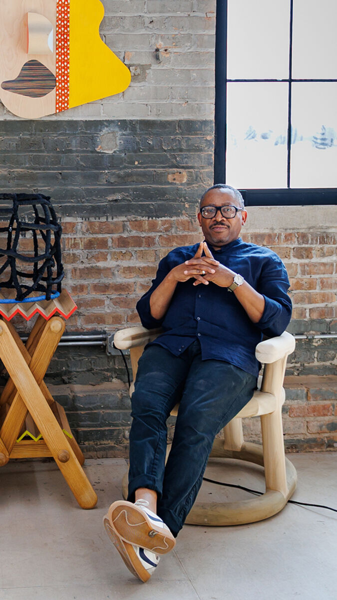 An artist sits in a sculptural chair n his studio