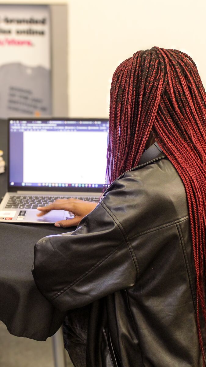 Three people seated at a table, viewing a laptop and a cell phone. 
