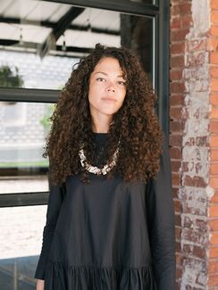  a portrait of a woman wearing a black dress in front of a brick exterior