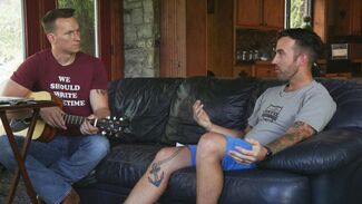 Two men sit on a couch with a guitar