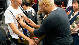 Performance art piece featuring audience members applying products to chest hair adhered to the artist's chest 