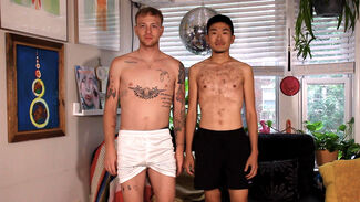 An Asian man and a white man standing next to each other indoors and both shirtless