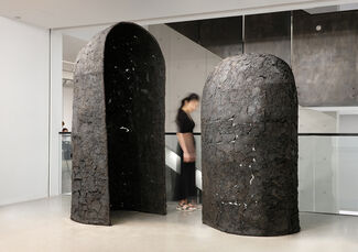 Person standing between two elements of a sculptural artwork in a gallery space