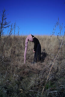 A person wearing a sculptural mask in a grassy outdoor area