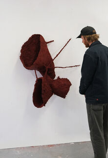 An adult person viewing a sculptural artwork hanging on the wall in a gallery space