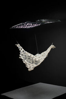 Abstract monochromatic sculpture suspended from ceiling in a black gallery space 