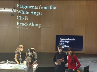 People standing in a wood-paneled room with the words "Fragments from the White Angst Cli-Fi Read-Along" projected on the wall